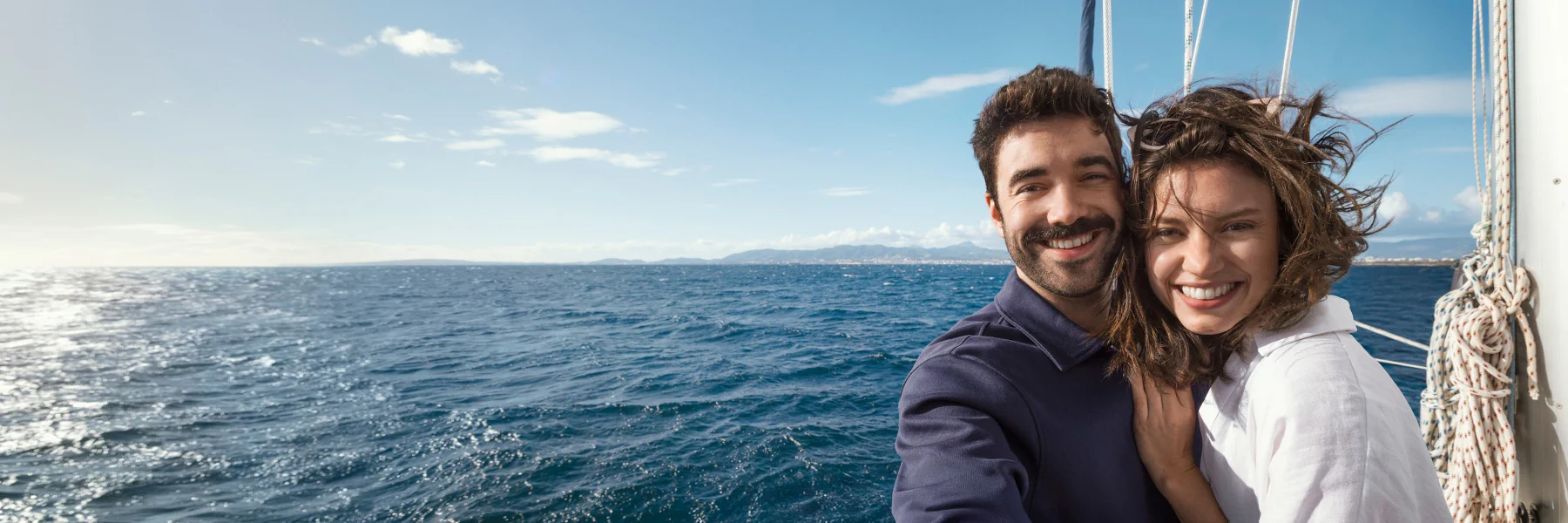 Paar auf einem Segelschiff. Im Hintergrund eine Küstenlinie am Horizont.